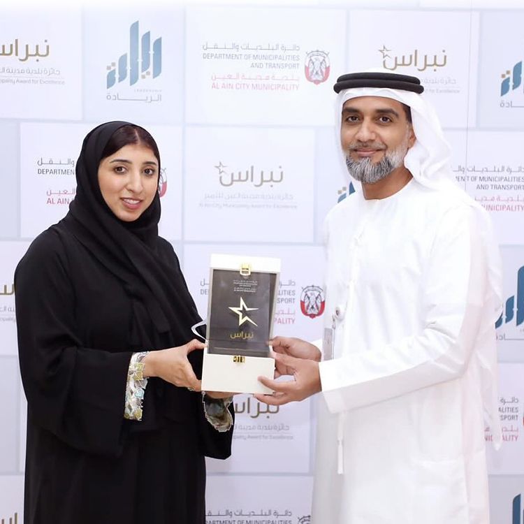 A woman smiling into the camera while being presented with an award by a man