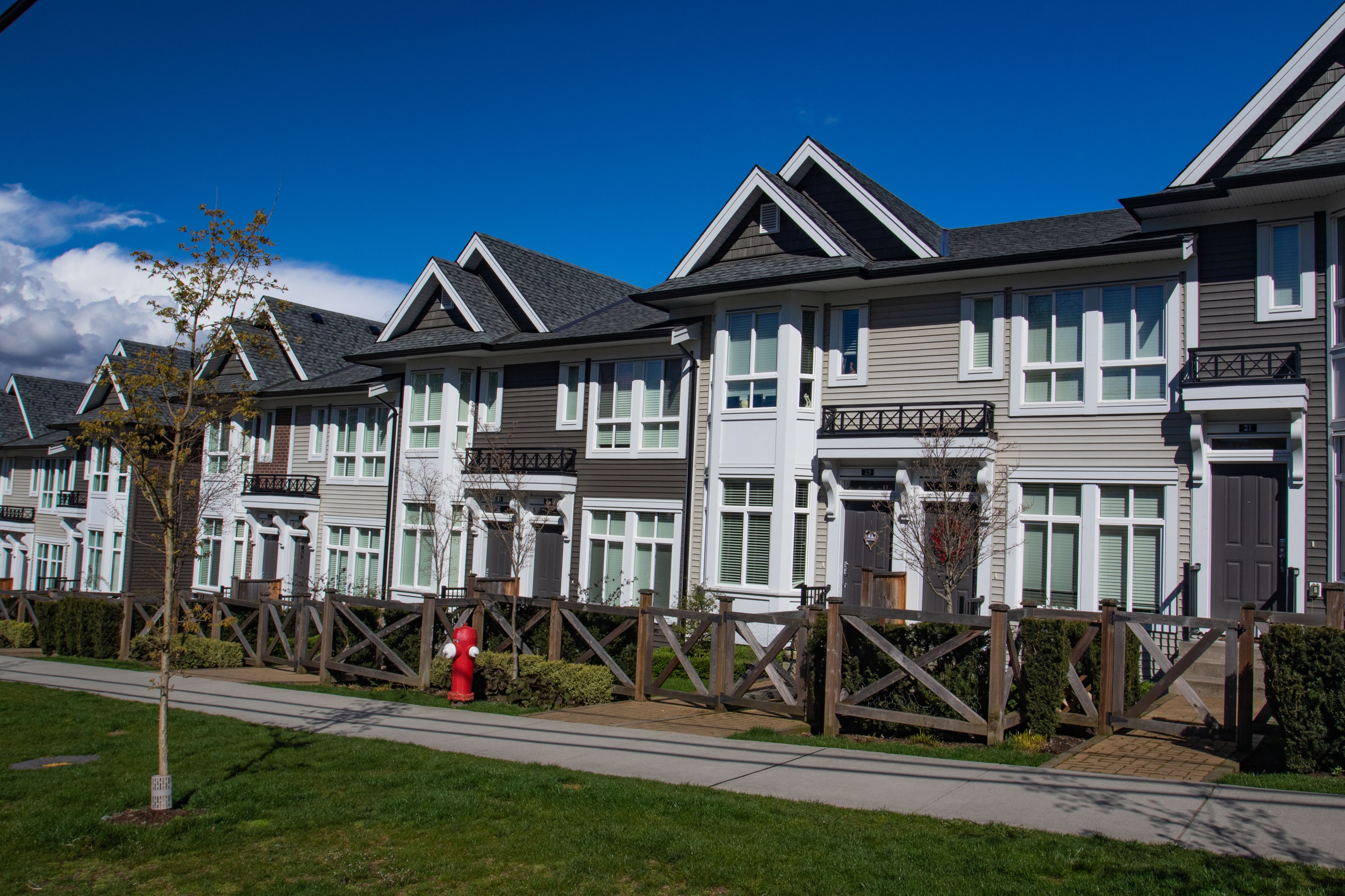 Row of new townhomes in a sidewalk neighbourhood on a sunny day in Canadian springtime against bright blue sky