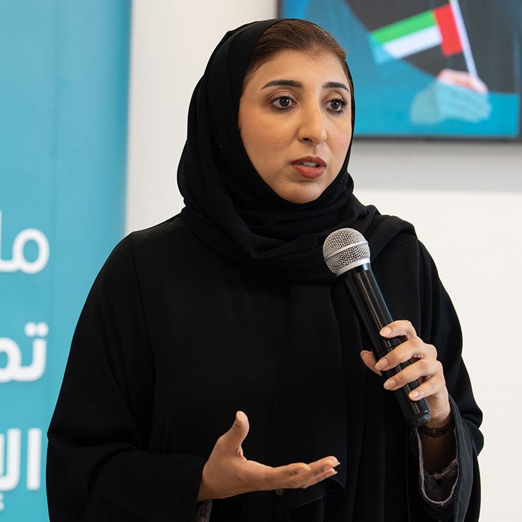 Woman holding a microphone and speaking to a gathering of women