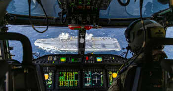 View looking out through a cockpit window at a warship below