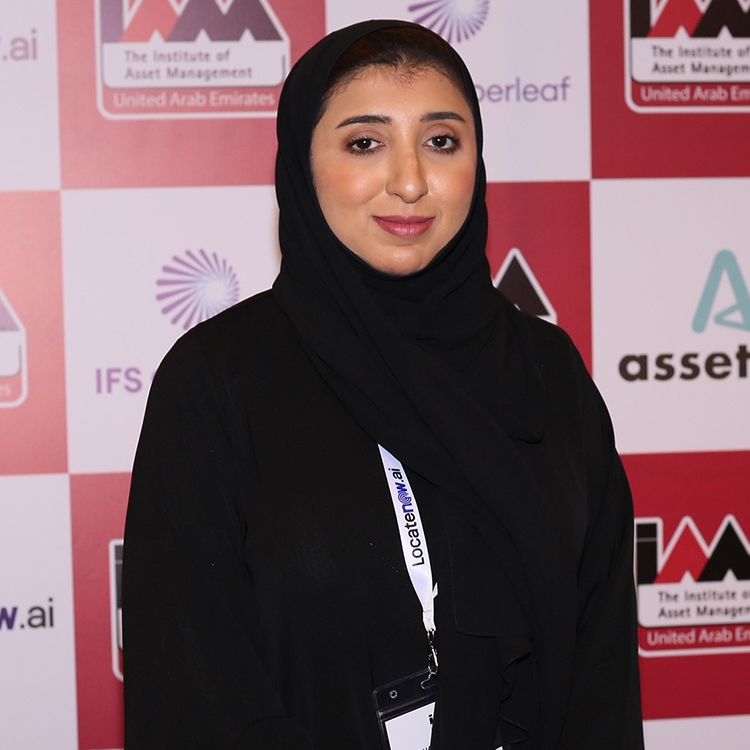 A woman smiling into camera with a backdrop showing the IAM UAE Chapter logo