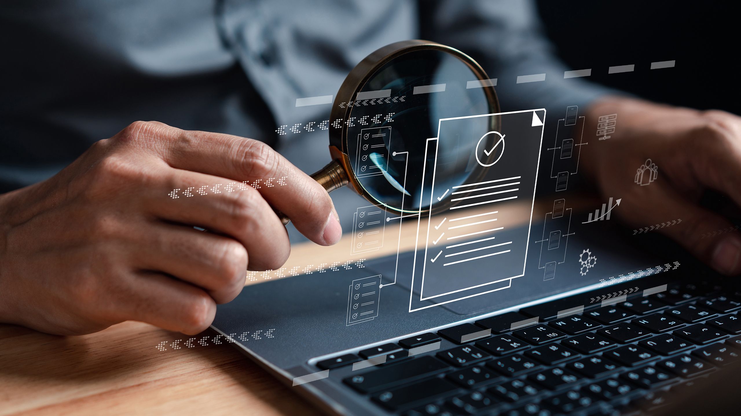 Image of hands holding a magnifying glass to look at charts projected from a laptop screen