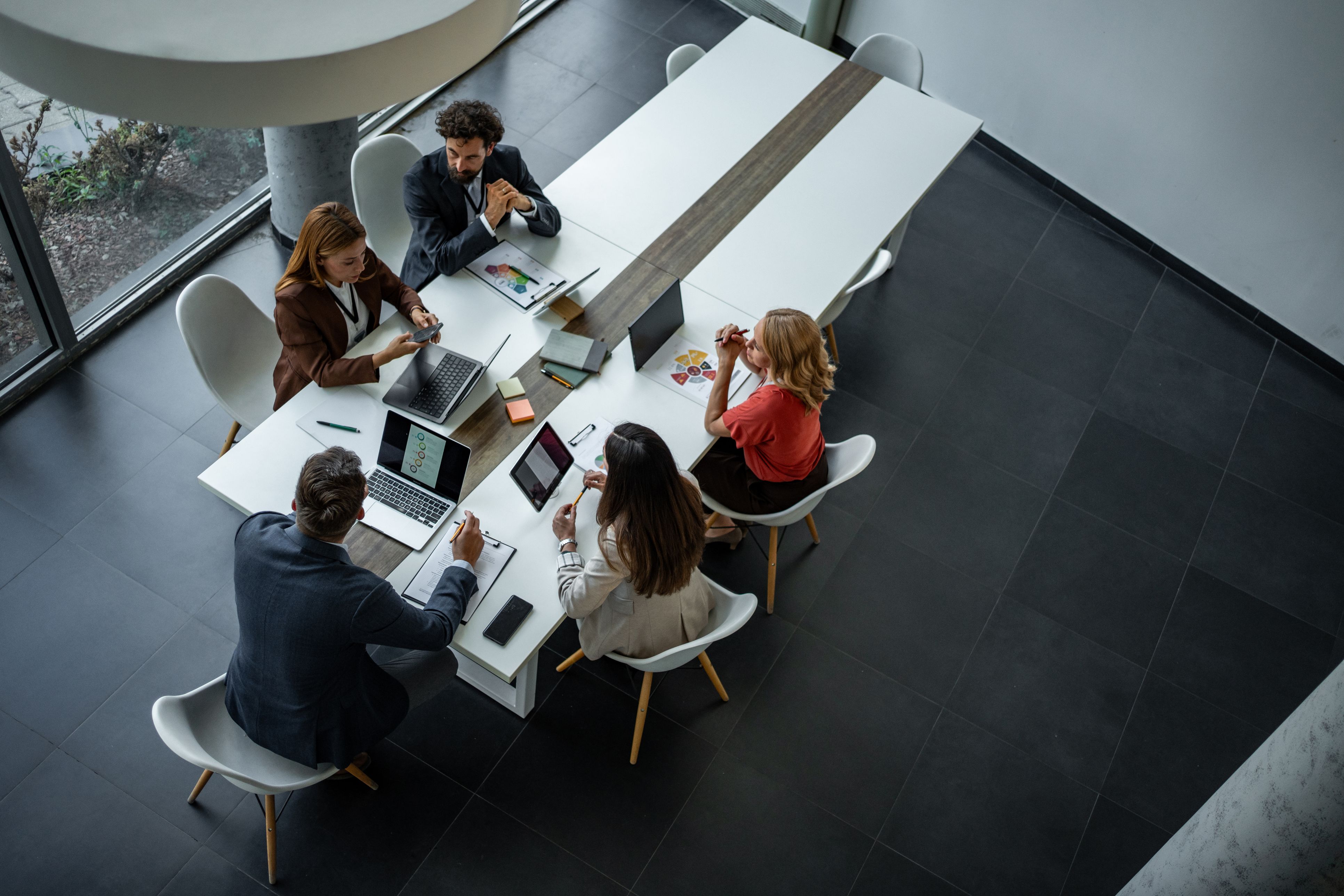 Image looking down on people in a business meeting with their laptops open on the table in front of them