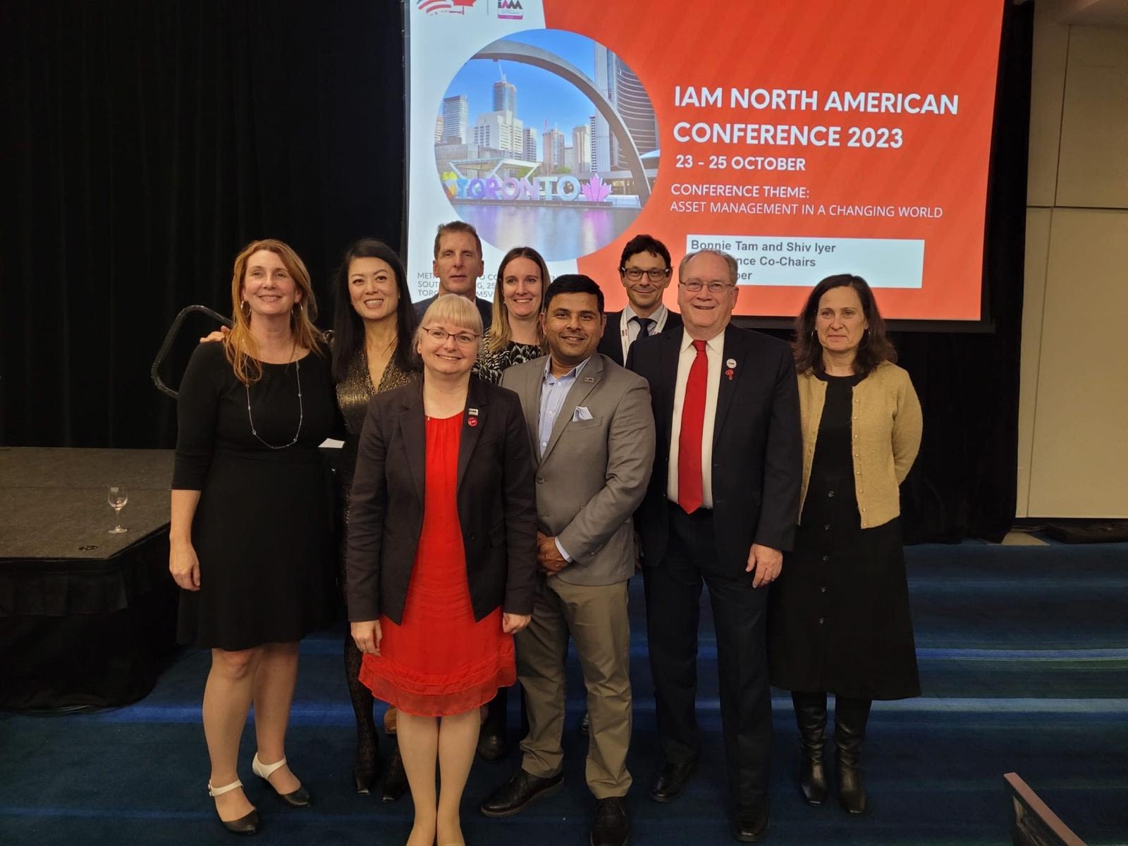Group of people smiling into camera with an IAM North American conference 2023 banner in the background